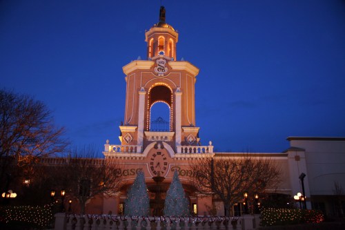 A beautifully lit building at dusk, featuring a clock tower and festive decorations, with trees in the foreground.