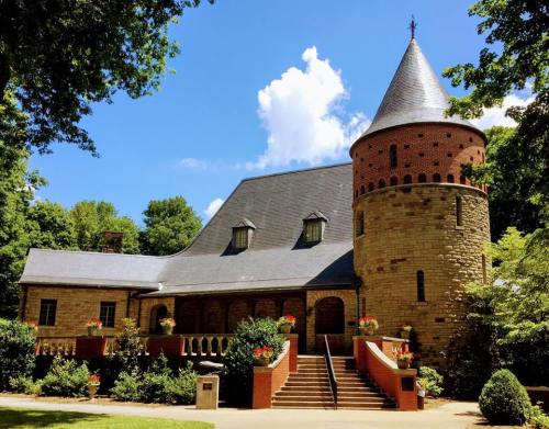 A charming stone castle with a conical tower, surrounded by lush greenery and colorful flower pots.