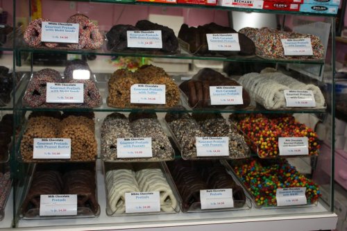 A display case filled with various chocolate-covered treats, including pretzels and candies, labeled with prices.