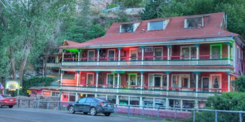 A colorful, multi-story building with a red roof and balconies, surrounded by greenery and parked cars.
