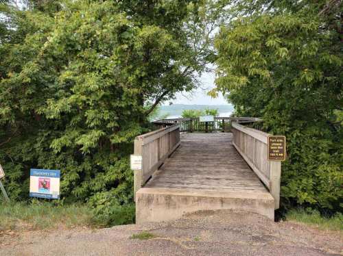 A wooden observation deck surrounded by trees, leading to a view of the water, with informational signs nearby.