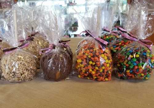 A display of caramel apples wrapped in clear plastic, decorated with ribbons and colorful toppings, on a table.