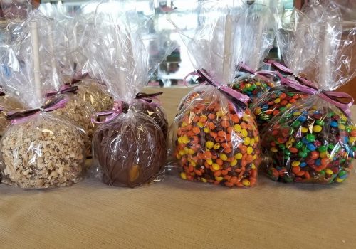 A display of caramel apples wrapped in clear plastic, decorated with ribbons and colorful toppings, on a table.