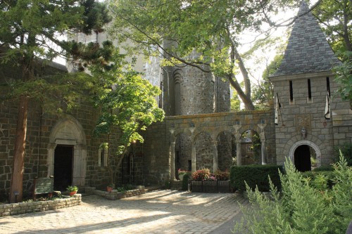 A stone building with towers and arches, surrounded by trees and greenery, creating a serene, historic atmosphere.
