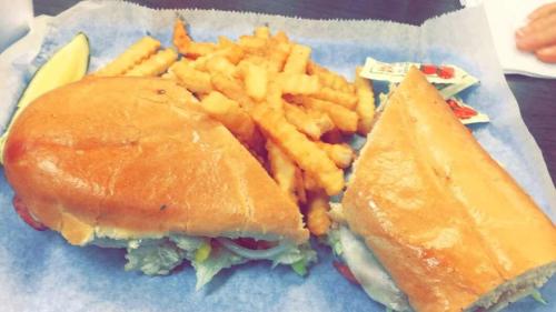 A sandwich with lettuce and tomato, served with crinkle-cut fries and two packets of sauce on a blue paper tray.