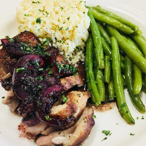 A plate featuring sliced roasted duck with a rich sauce, served with rice and green beans, garnished with herbs.