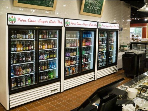 Three glass-front vending refrigerators filled with various soda bottles and cans in a store setting.