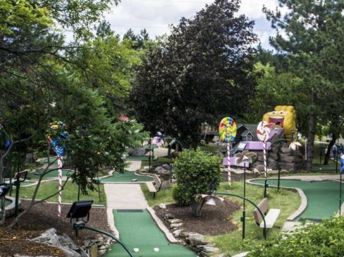 A colorful mini-golf course with candy-themed decorations and lush greenery in the background.