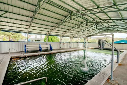 Indoor swimming pool with a covered roof, featuring a slide and seating area, surrounded by greenery.