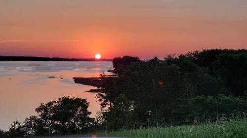 A serene sunset over a calm lake, with silhouettes of trees along the shore and a colorful sky.