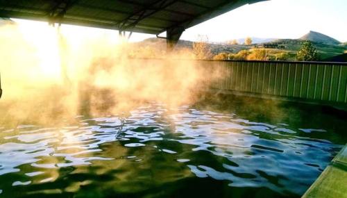A serene pool with steam rising, surrounded by a scenic landscape at sunset.