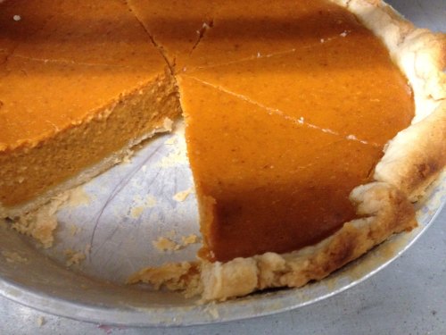 A pumpkin pie with a slice removed, showing a smooth, orange filling and a golden-brown crust in a metal pie pan.