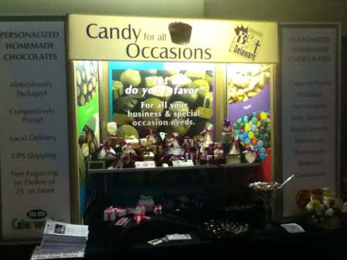 A display booth featuring various homemade chocolates and candies, with promotional signage for special occasions.