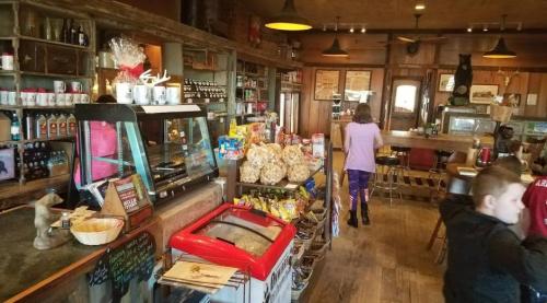 Cozy café interior with a display case, snacks, and wooden decor; a child and an adult are seen in the background.