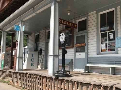 A rustic building with a restaurant sign, a coin-operated viewer, and an ice vending machine on a wooden porch.