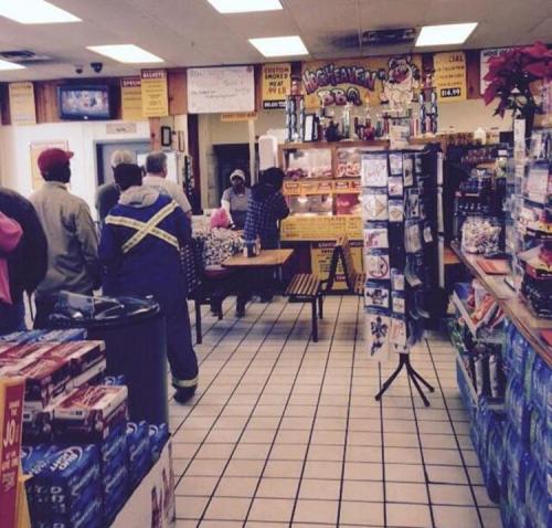 A busy convenience store interior with customers at the counter and shelves stocked with various products.