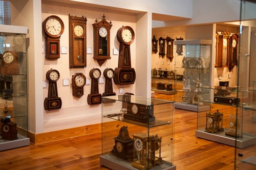 A museum display featuring various antique clocks on walls and in glass cases, showcasing intricate designs and craftsmanship.