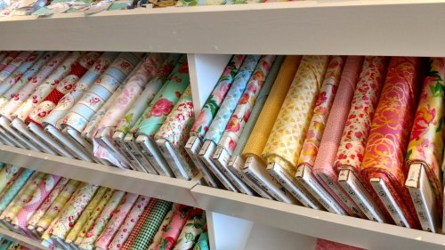 Colorful rolls of fabric neatly arranged on shelves, featuring floral and geometric patterns in various shades.