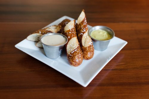 A plate of soft pretzels with two dipping sauces, one creamy and one mustard, on a wooden table.