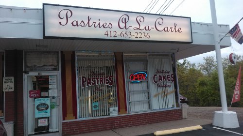 A storefront for "Pastries A-La-Carte" featuring an "OPEN" sign and displays of pastries and cakes.