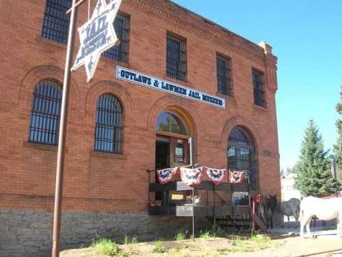 Historic brick building with barred windows, featuring a sign for the Outlaws & Lawmen Jail Museum and decorative bunting.