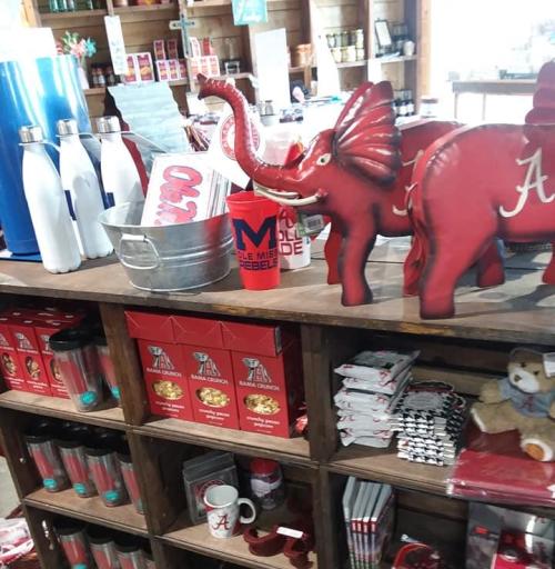 A display of red Alabama-themed merchandise, including cups, a bucket, and elephant figurines, in a store setting.
