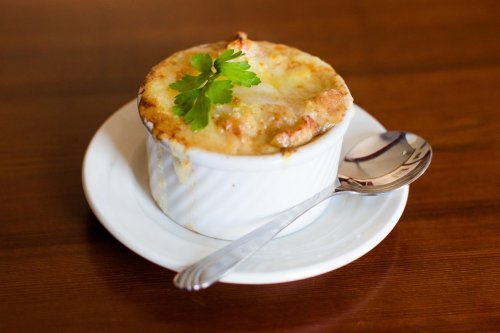 A bowl of baked French onion soup topped with melted cheese and a sprig of parsley, served on a white plate with a spoon.