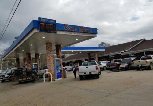 A gas station with a blue and white sign displaying fuel prices, surrounded by parked trucks and cloudy skies.