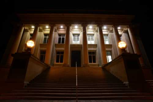 A grand building with tall columns and illuminated steps, viewed at night. Soft light from lamps enhances its architecture.