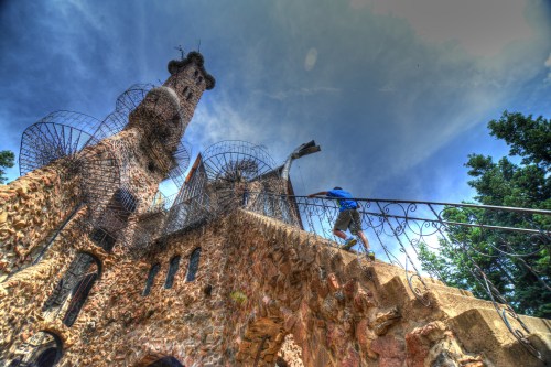 A person climbs stairs of a unique stone structure with towers and intricate metalwork against a dramatic sky.