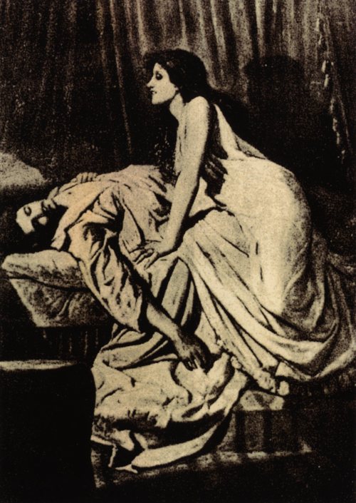 A woman in a flowing dress leans over a reclining figure on a bed, creating a dramatic and intimate scene.