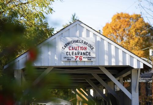 Sign on a covered bridge reads "Caution Clearance 7' 6" with autumn trees in the background.