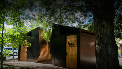 Modern architectural structure with wooden doors, surrounded by greenery and trees.