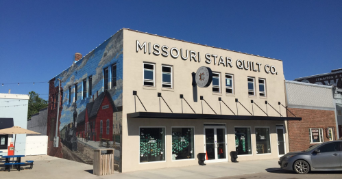 Exterior of the Missouri Star Quilt Co. building, featuring a mural and large signage, in a sunny urban setting.