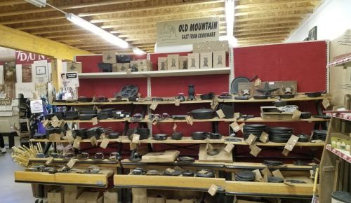 Display of various cast iron cookware and kitchen items on wooden shelves in a store.