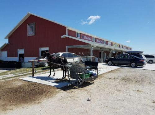 A horse and cart are parked outside a red barn-style building on a sunny day.