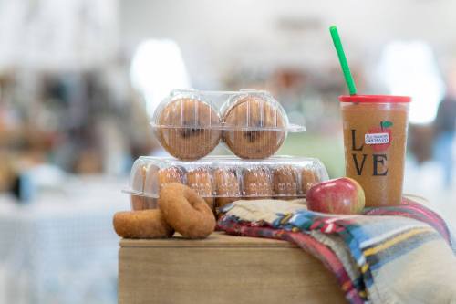 A display of muffins, donuts, and a drink on a table with a plaid cloth and an apple.