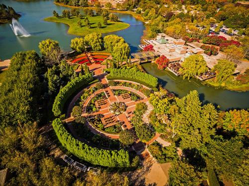 Aerial view of a landscaped park featuring circular gardens, a pond, and colorful trees in autumn.