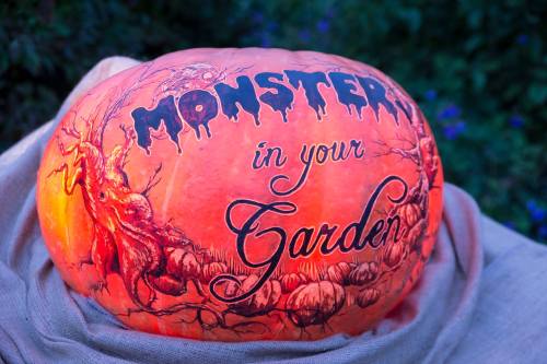 A carved pumpkin with the words "Monsters in your Garden" illuminated, set against a dark, leafy background.