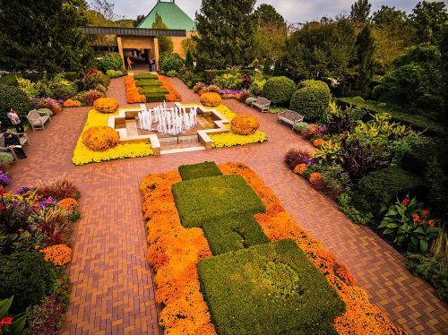 A vibrant garden with colorful flowers, neatly arranged hedges, and a central fountain surrounded by benches.