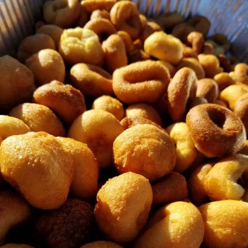 A close-up of a pile of golden-brown mini donuts, varying in size and shape, arranged in a tray.