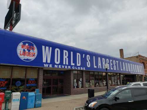 A large blue sign on a laundromat reads "WORLD'S LARGEST LAUNDROMAT" with the slogan "WE NEVER CLOSE."