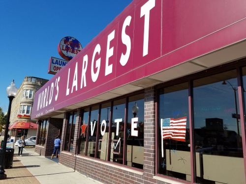 Exterior of a building with a sign reading "World's Largest," featuring a "Vote" display and an American flag in the window.