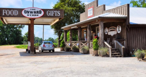 A rustic store with a sign reading "The Onward Store," featuring a porch and a car parked outside.