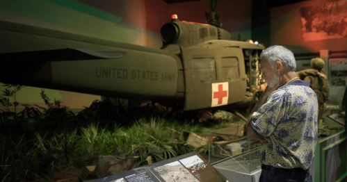 A visitor examines a military helicopter display in a museum, with informational panels nearby.