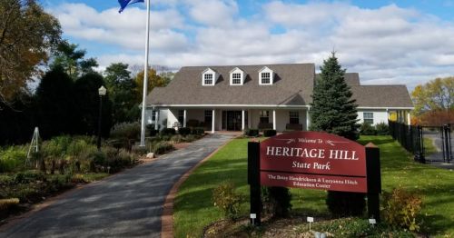 A welcoming entrance to Heritage Hill State Park, featuring a building, flag, and landscaped pathway.