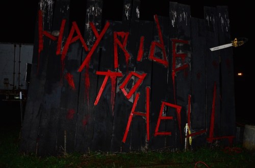 A dark wooden sign with red letters reading "Hayride to Hell," set against a nighttime background.