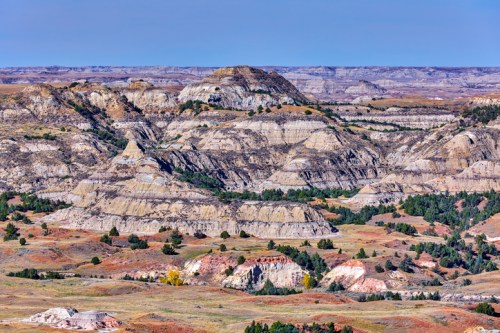 A panoramic view of layered hills and valleys in a rugged landscape under a clear blue sky.