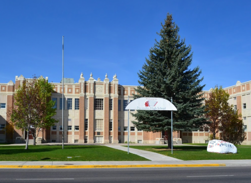 Exterior view of Pocatello High School, featuring a large tree and a sign for Homecoming Week in front.