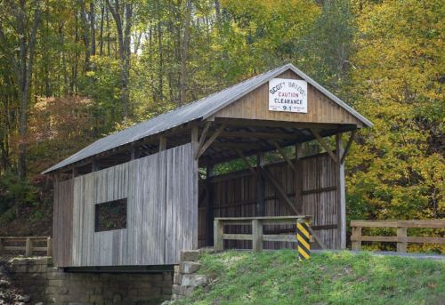 A wooden covered bridge with a sign reading "Scott Bridge" surrounded by autumn foliage and trees.